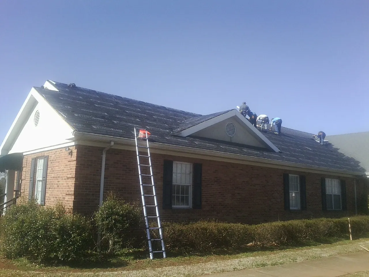 Crew tearing shingles off a brick ranch roof with a ladder set — Emergency Roof Repair work by our crew in Slade