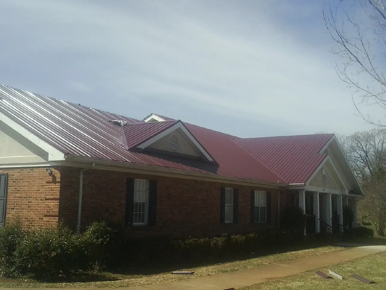 Red metal roof with gabled entries on a long brick building, from a Hail Damage Roof Repair job in Slade