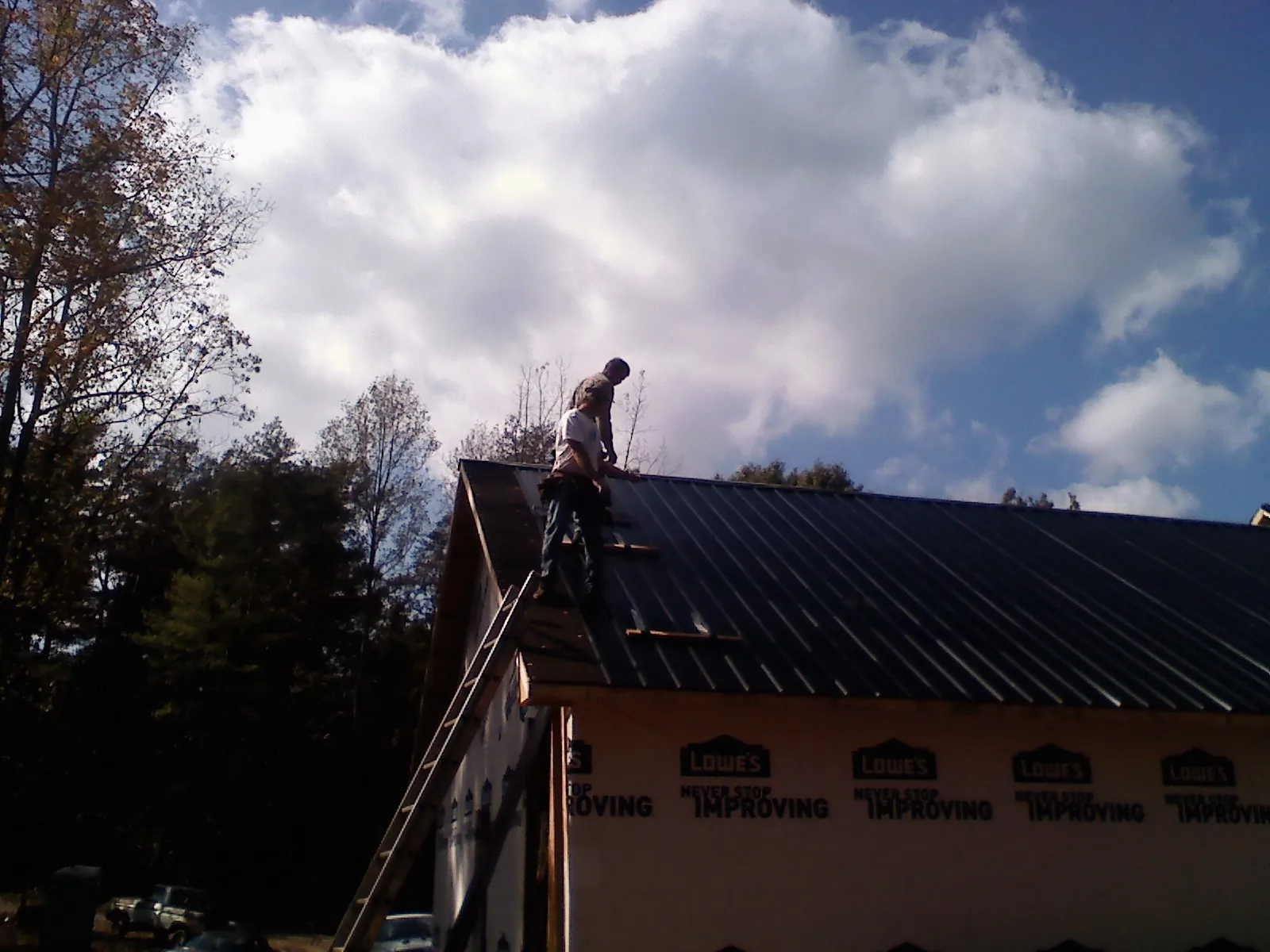 Roofer fastening dark metal panels high against a cloudy sky, from a Roof Inspection job in Slade