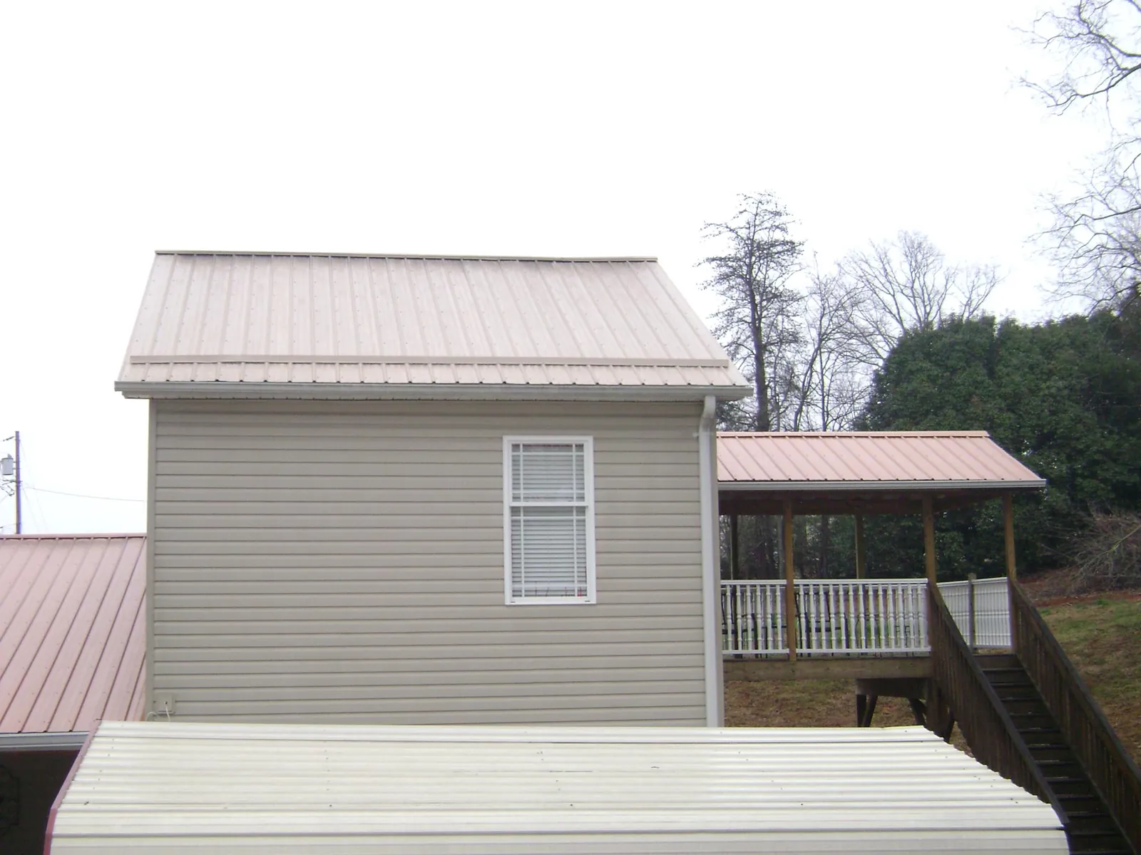 Tan metal roofs on a two story addition and attached porch, from a Roof Replacement job in Slade