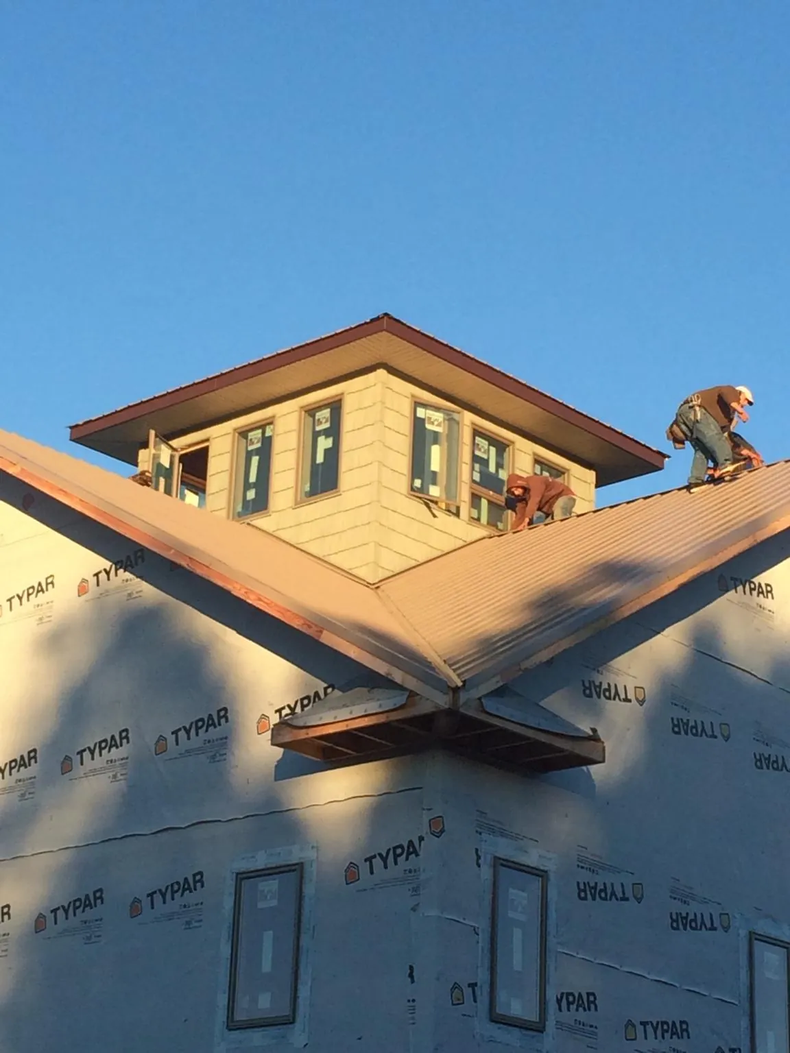 Roofers working around a rooftop cupola on a new metal roof at sunset — Roof Waterproofing in Slade by Roofing Brothers